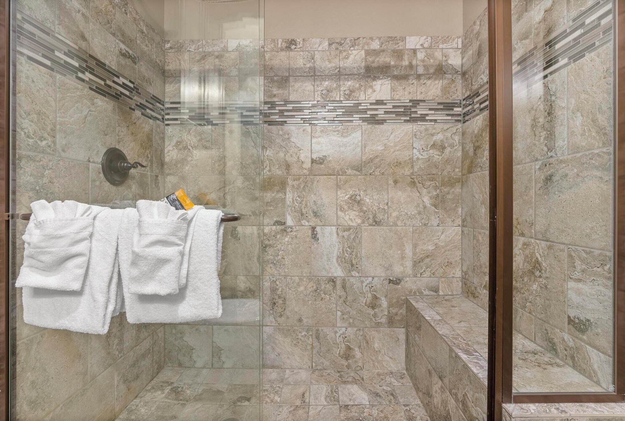 A shower with a glass door, marble tiles, and a towel rack with white towels.