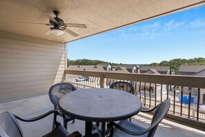 Ein Balkon mit einem runden Tisch und vier Stühlen, einem Deckenventilator und Blick auf ein Wohngebiet mit Häusern und Bäumen.