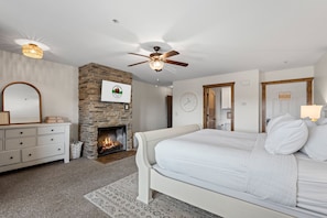 A bedroom with a stone fireplace, a bed, a dresser, a mirror, and a ceiling fan. - 2 Lake-View Balconies | Updated 2BR/2BA | Less Than 5 Min to Silver Dollar City (Branson)