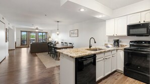 A modern kitchen with white cabinets, a black dishwasher, and a granite countertop. - 2 bd/2ba, Deck Space, Ticket Deals and 2 minutes to Silver Dollar City! (Branson)
