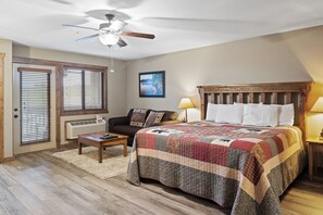 A bedroom with a large bed, a ceiling fan, a wooden headboard, a nightstand with a lamp, a wooden bench, a window with blinds, and a framed picture on the wall. - 2BD/2Ba Lake Community Condo, Resort Amenities, Ticket Deals Sleep up to 10! (Branson)