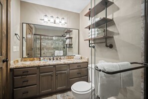 A bathroom with a marble countertop, wooden cabinets, a glass shower enclosure, and a towel rack. - 2BD/2Ba Lake Community Condo, Resort Amenities, Ticket Deals Sleep up to 10! (Branson)