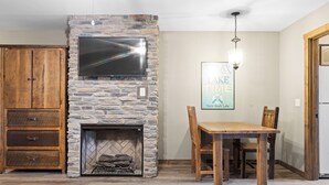 Una chimenea de piedra con un televisor montado arriba, una mesa de comedor con sillas, y un mueble de madera con cajones.