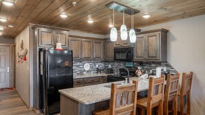A modern kitchen with granite countertops, wooden cabinets, a black refrigerator, a stainless steel sink, and a built-in island with bar stools.