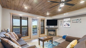 A modern living room with a fireplace, a television, and a ceiling fan.