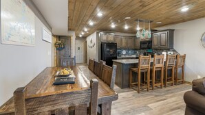A modern kitchen with wooden cabinets, a central island with bar stools, and a dining area with a wooden table and chairs.