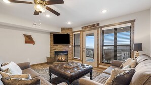 Una sala de estar con chimenea, sofás de cuero, ventilador de techo y un ventanal grande.