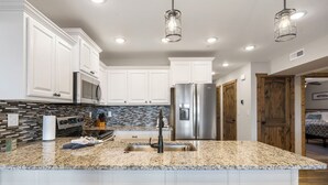 Una cocina moderna con armarios blancos, electrodomésticos de acero inoxidable, encimera de granito y una zona de bar con taburetes.