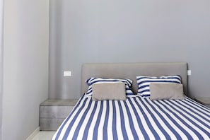 A bed with striped bedding, a grey headboard, and a bedside table.