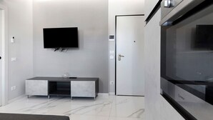 Una habitación moderna con un televisor de pantalla plana montado en la pared, un mueble empotrado para entretenimiento, una puerta y un horno o microondas de gran tamaño.
