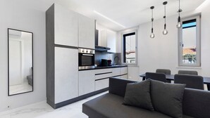 Una cocina moderna con electrodomésticos integrados, un comedor con mesa y sillas, y un sofá gris con cojines.