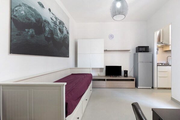 Una habitación compacta con cama, televisor, kitchenette y un cuadro grande en la pared.