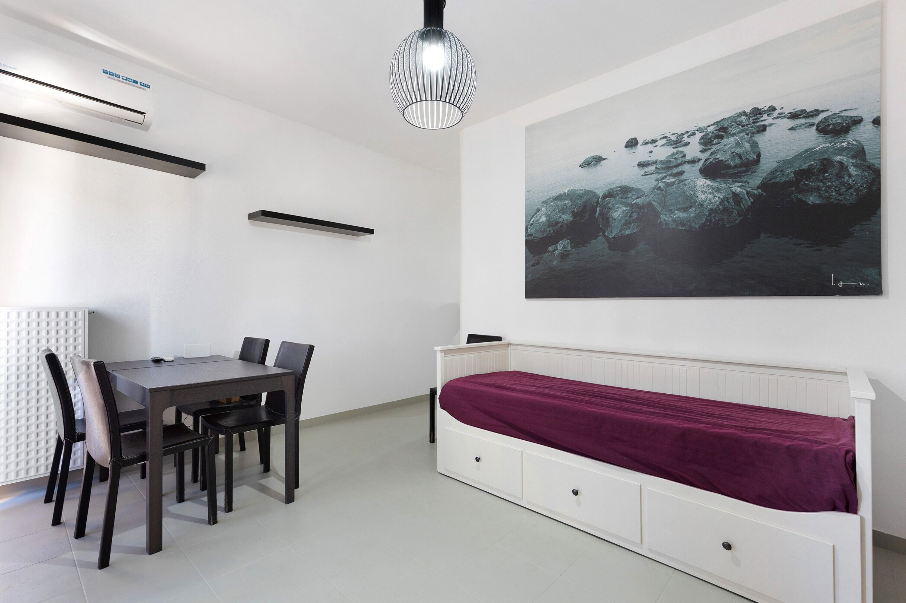 Una habitación moderna con una mesa de comedor, sillas, una cama blanca, un radiador y un cuadro grande de rocas.