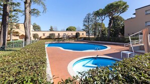 Una piscina de diseño curvo, rodeada de setos y árboles, con edificios al fondo.
