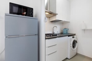 A compact kitchen with a refrigerator, microwave, stove, sink, and washing machine.