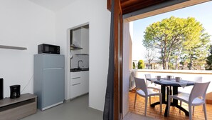 Cocina compacta con microondas, refrigerador y comedor con sillas y mesa.