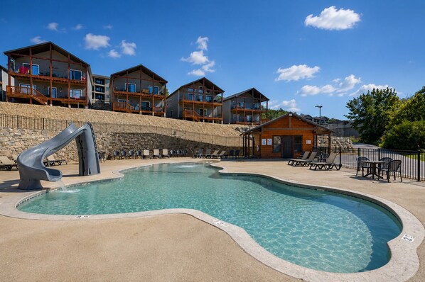 Une piscine avec un toboggan, des chaises longues et un chalet en bois.