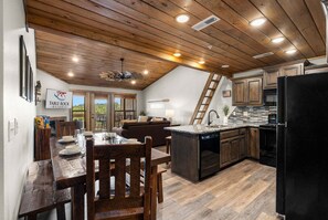 A modern kitchen with wooden ceiling beams, a dining area with a table set for four, and a view of the outdoors. - Morning Coffee with Lake Views Starts Here (Branson)