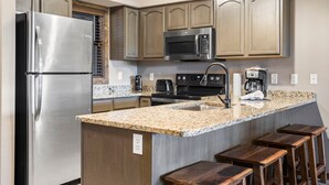 Eine moderne Küche mit Edelstahlgeräten, Granitarbeitsplatten, Holzsäulen und Barhocker.