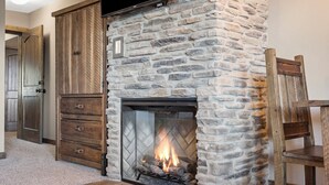 A stone fireplace with a fire, a wooden cabinet, and a chair. - Studio Condo overlooking Table Rock Lake, 2 min to SDC, Ticket Deals, Resort Perks! (Branson)
