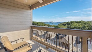 A balcony with a view of a lake and forest, a ceiling fan, and a chair. - Studio Condo overlooking Table Rock Lake, 2 min to SDC, Ticket Deals, Resort Perks! (Branson)
