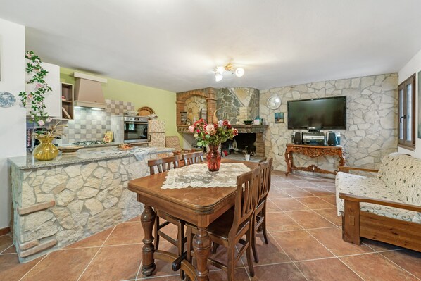 A stone kitchen with a dining table, chairs, and a TV.