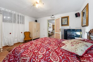 A bedroom with a large bed, a chair, a wardrobe, a mirror, and a door leading to another room.