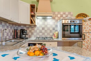 A kitchen with a gas stove, oven, sink, and a bowl of fruit on the counter.