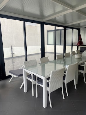 Un espace repas moderne avec une table en verre, des chaises en osier blanc et de grandes fenêtres offrant une vue panoramique.