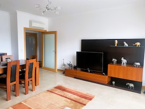 Un salon avec un téléviseur, des meubles en bois, un tapis et des objets décoratifs disposés sur des étagères.