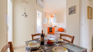 Un coin repas avec une table dressée pour deux personnes, une bouteille de vin et un saladier de fruits.