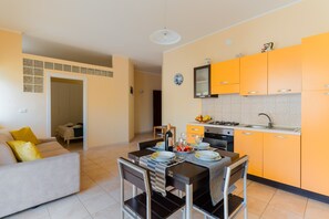 Une cuisine moderne avec des meubles de couleur jaune, une table à manger dressée pour deux personnes et un canapé dans le salon attenant.