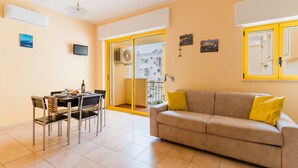 A living room with a sofa, a dining table with chairs, a TV, and a sliding glass door leading to an outdoor balcony. - Holiday Home 'Anthea in Otranto' with Balcony, Wi-Fi, and Air Conditioning (Otranto)