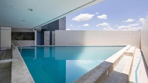 A modern indoor swimming pool with clear blue water, a concrete edge, and a view of the sky.