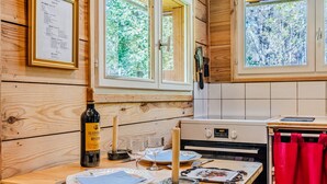 Un intérieur en bois comprenant un coin cuisine, une table à manger dressée avec des assiettes, des verres et une bouteille de vin Madir.