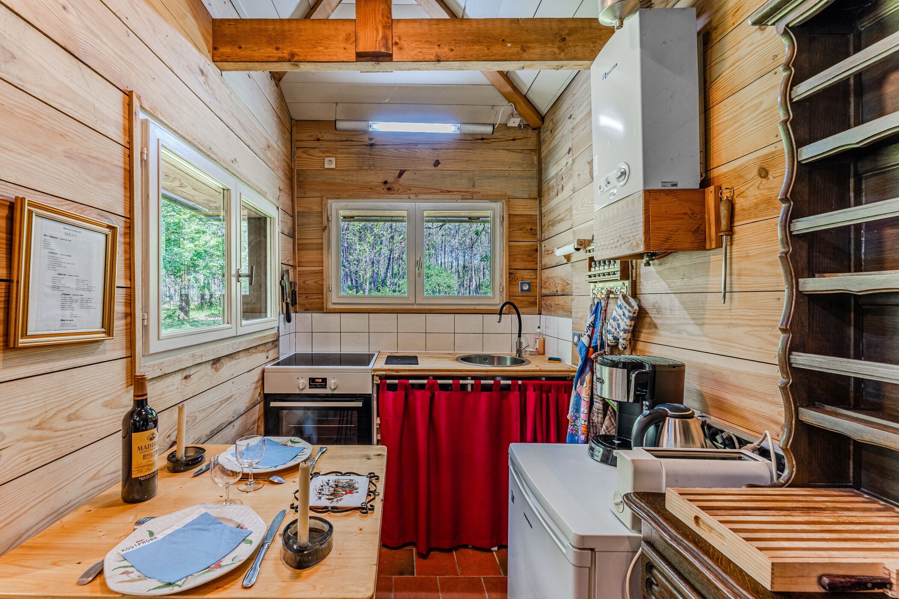 L’intérieur d’un chalet en bois comprend une cuisine, un coin repas et deux fenêtres donnant sur la forêt.