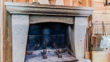 A stone fireplace with a metal grate, a rustic wooden wall, and a metal rack with tools.