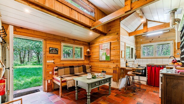 L’intérieur d’un chalet en bois comprend une table à manger, un canapé, un coin cuisine et de grandes fenêtres.