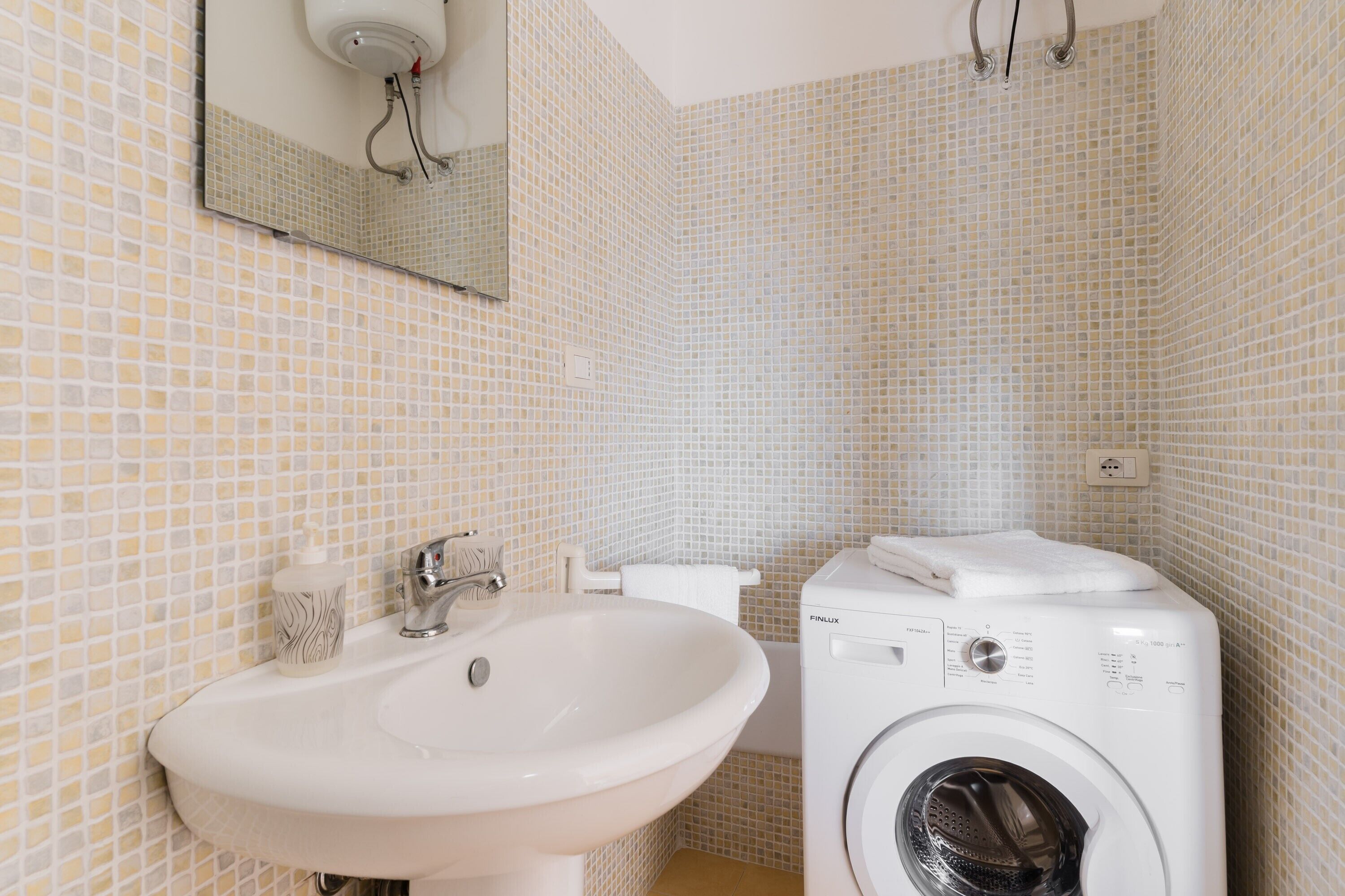 Un baño con lavabo, espejo, inodoro y lavadora.