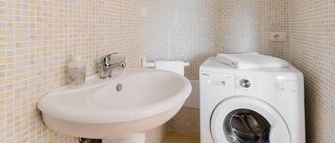 Un baño con lavabo, espejo, inodoro y lavadora.