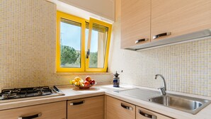 Une cuisine avec des meubles de rangement en bois, une cuisinière à gaz, un évier et une fenêtre aux cadres jaunes.