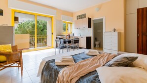 Une chambre à coucher avec un lit, un bureau et une chaise. Il y a un balcon avec vue sur les arbres.