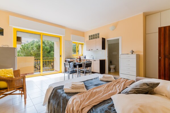 Une chambre à coucher avec un lit, un bureau et une chaise. Il y a un balcon avec vue sur les arbres.