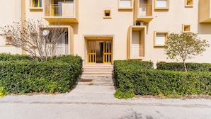 Un immeuble résidentiel à plusieurs étages, doté d’une entrée centrale, de balcons et d’une haie bien entretenue.