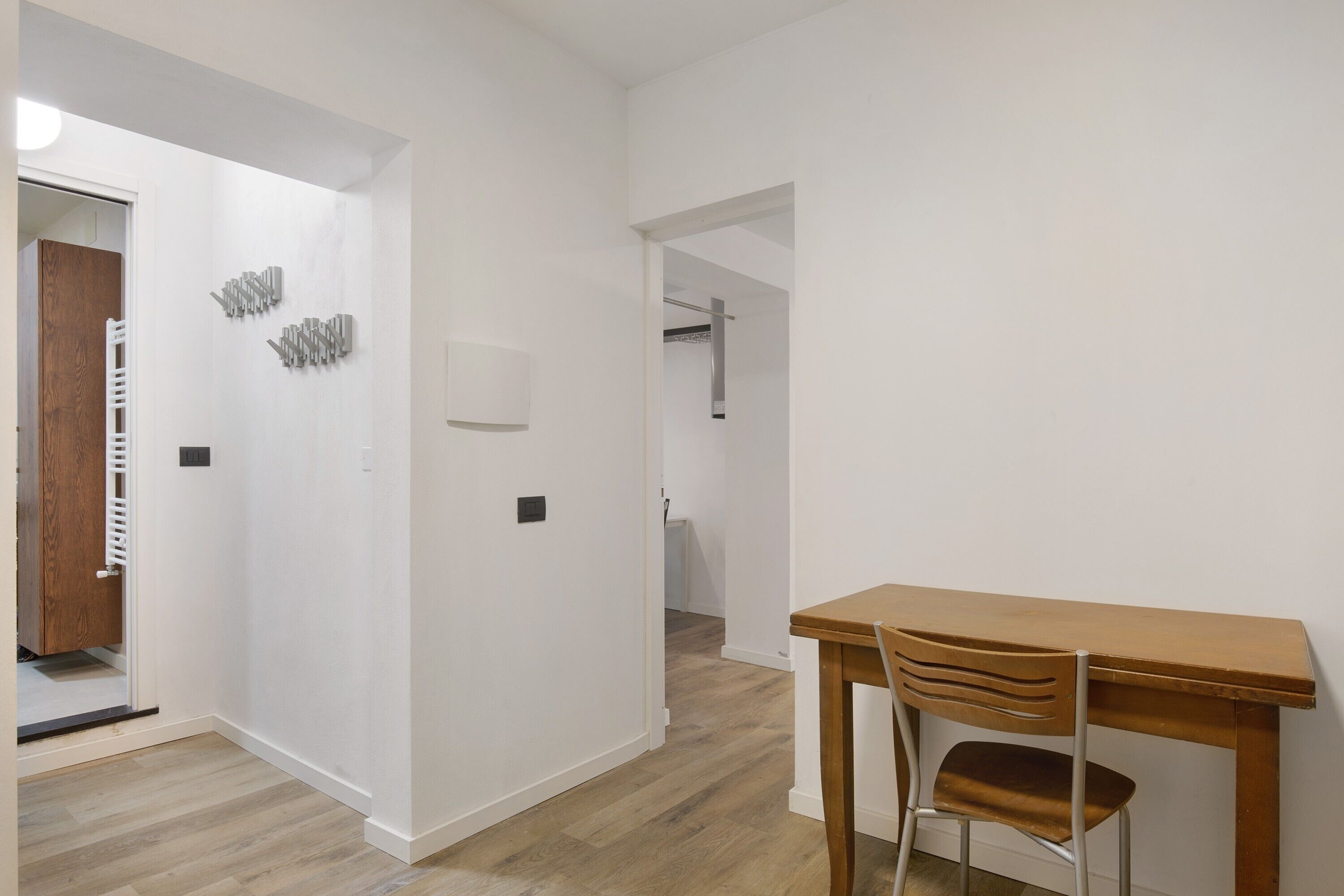 A hallway with a wooden door, a coat rack, and a table with a chair.