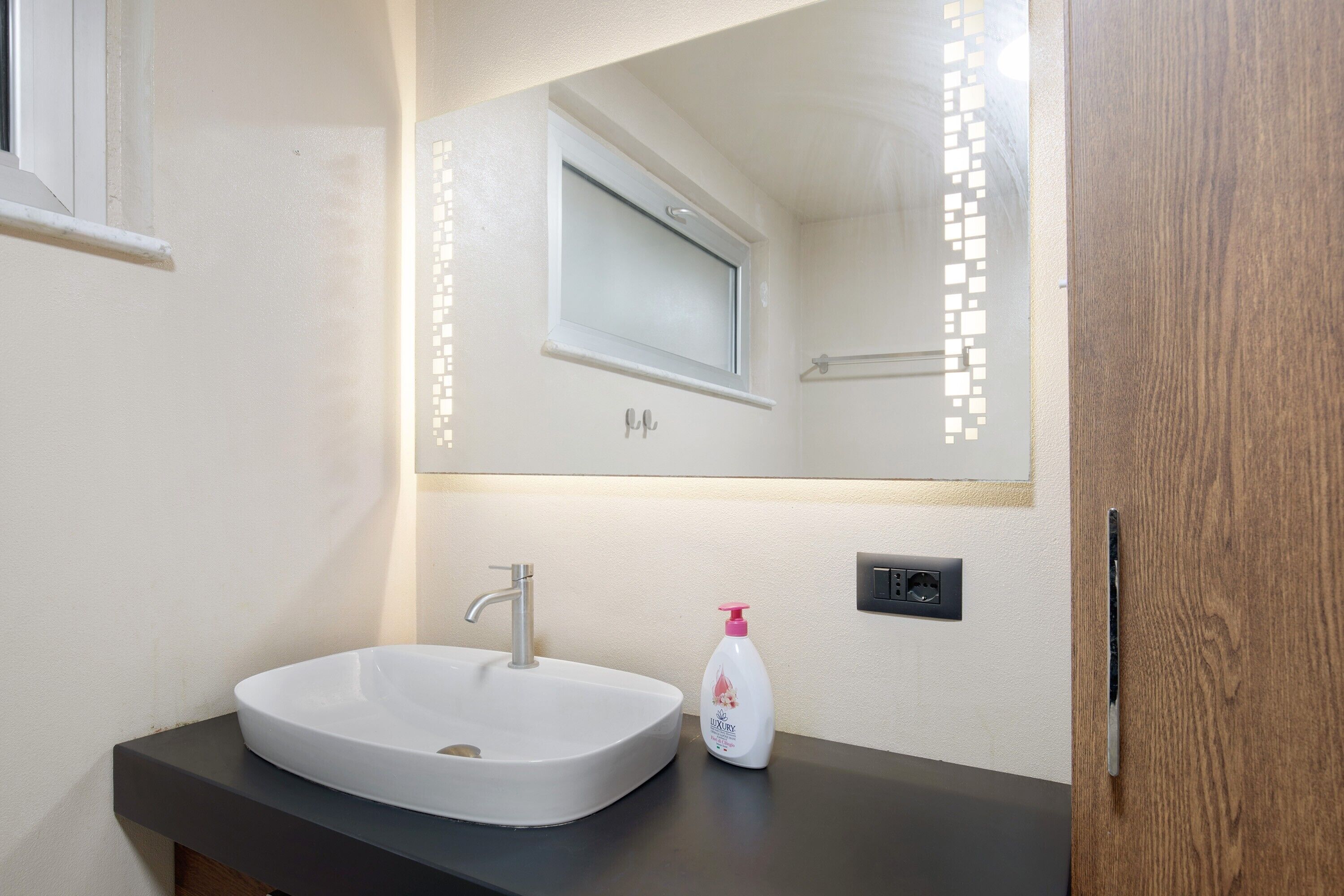 Ein Badezimmer mit einem weißen Waschbecken, einem Spiegel und einer Lotionflasche.
