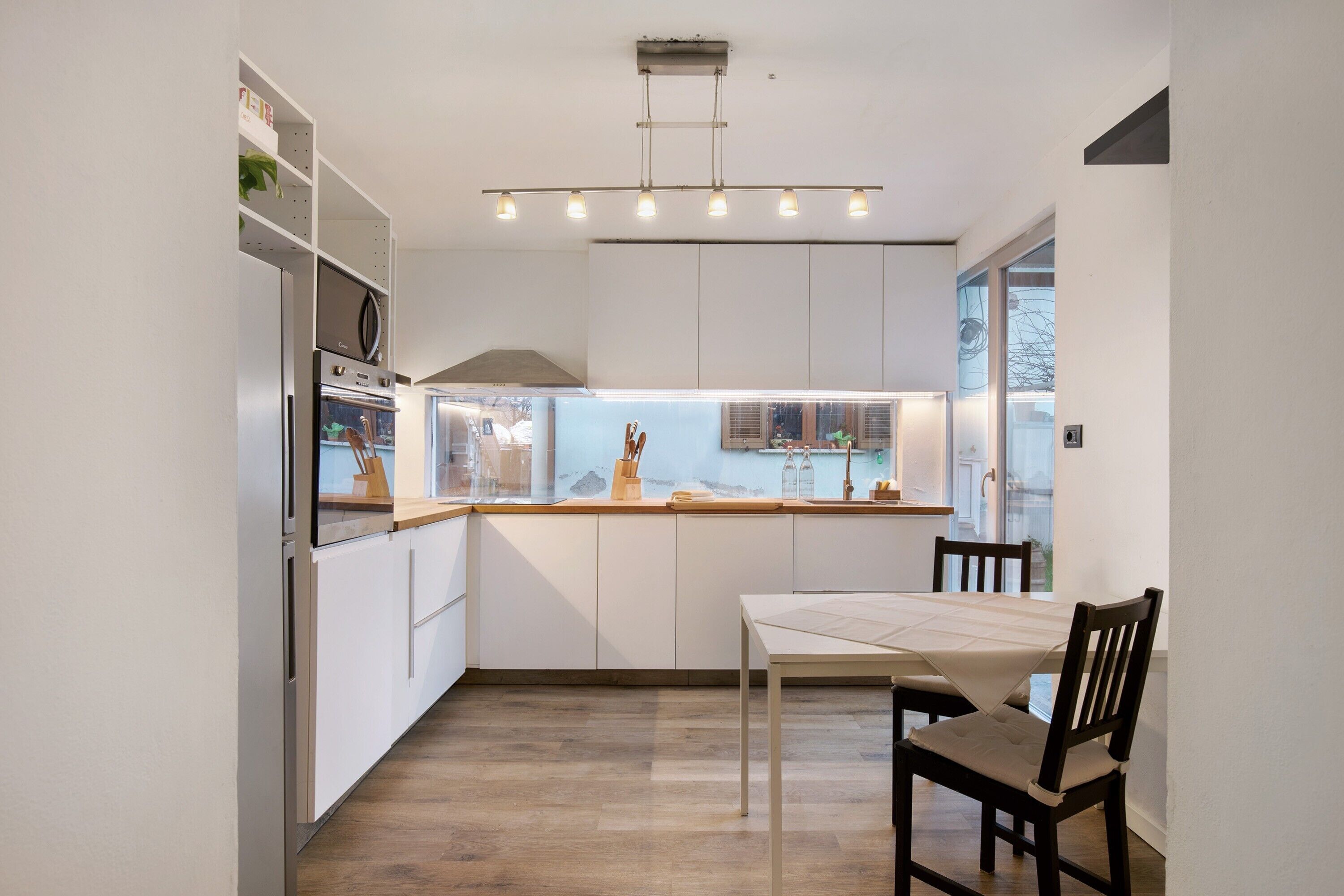 A modern kitchen with white cabinetry, a built-in oven, and a dining area with a table and chairs.