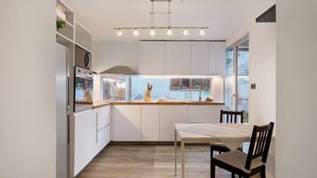 A modern kitchen with white cabinetry, a built-in oven, and a dining area with a table and chairs.