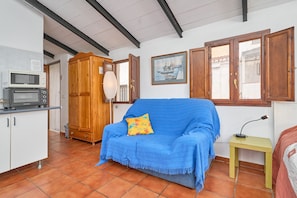 Una habitación con kitchenette, un sofá azul, un armario de madera y un cuadro en la pared.
