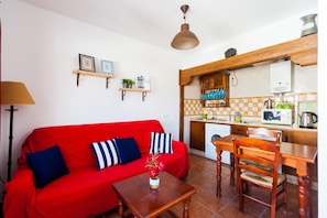 Un divano rosso con cuscini a righe, un tavolo da pranzo in legno e un angolo cottura con forno a microonde e lavello.